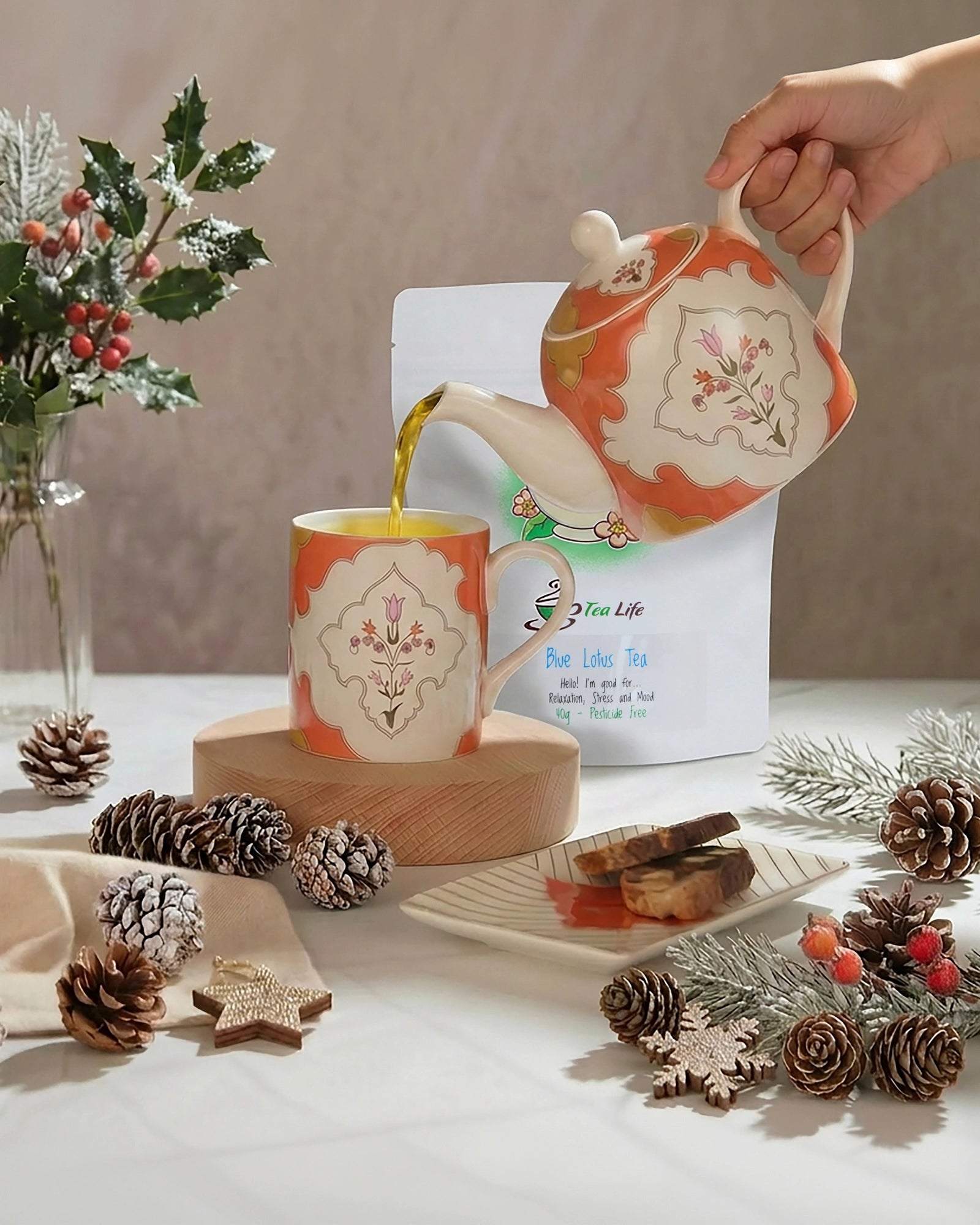 Tea being poured from a decorative teapot into a matching mug on a table with festive decorations.