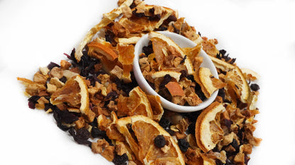 A pile of dried citrus and berry tea mix with a small white bowl in the center, photographed on a plain white background.

