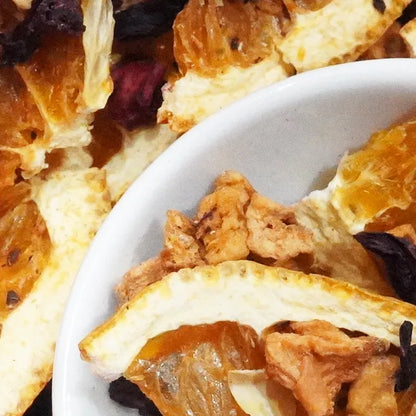 Close-up of dried fruit slices and pieces in a white bowl, including orange peel, dried berries, and golden dried pieces.


